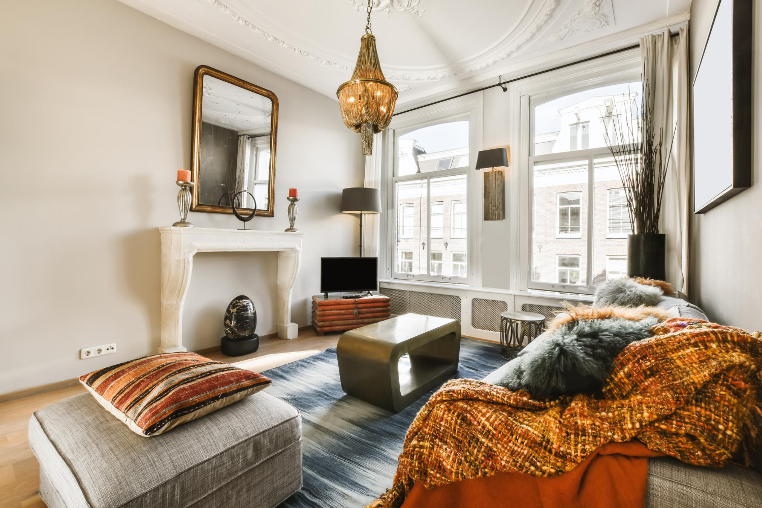 Eclectic living room with decorative fireplace, ornate ceiling, vintage chandelier, and large windows with natural light